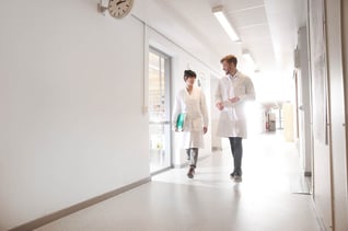 Svar-Life-Science-laboratory-technicians-in-lab-coats-carrying-green-folder-walking-in-long-bright-corridor