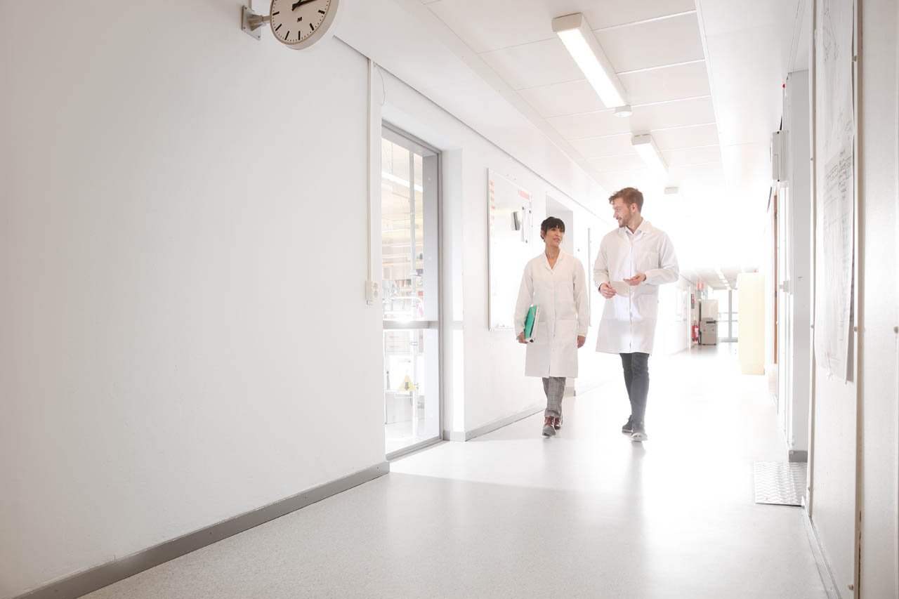 Svar-Life-Science-laboratory-technicians-in-lab-coats-walking-in-long-bright-corridor